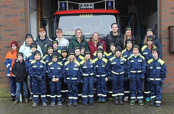 Jugendfeuerwehr-Gruppe in Uniform steht vor einem Feuerwehrfahrzeug in einer Fahrzeughalle
